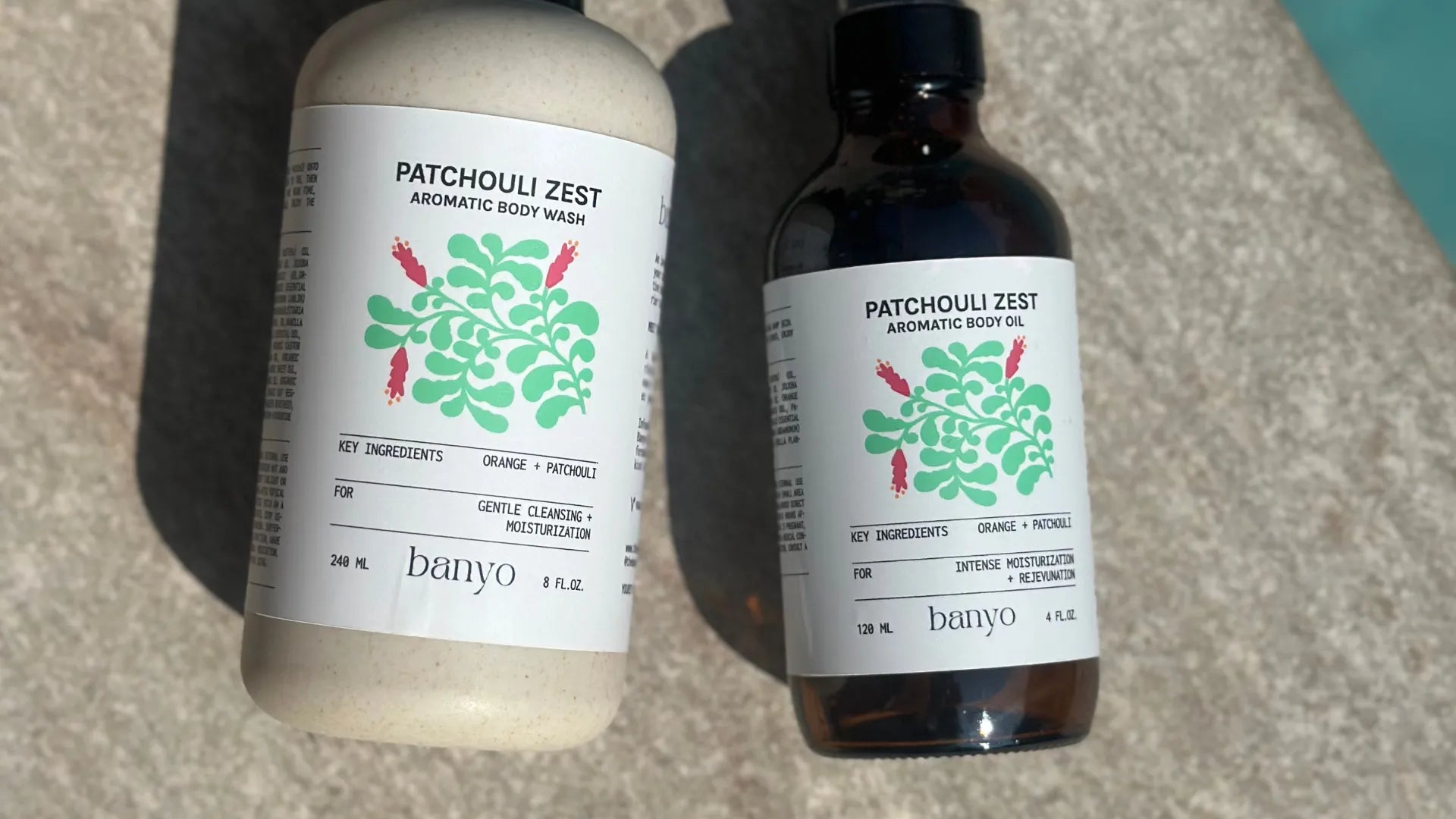 Two bottles of 'Patchouli Zest' body wash by banyo on a textured surface.